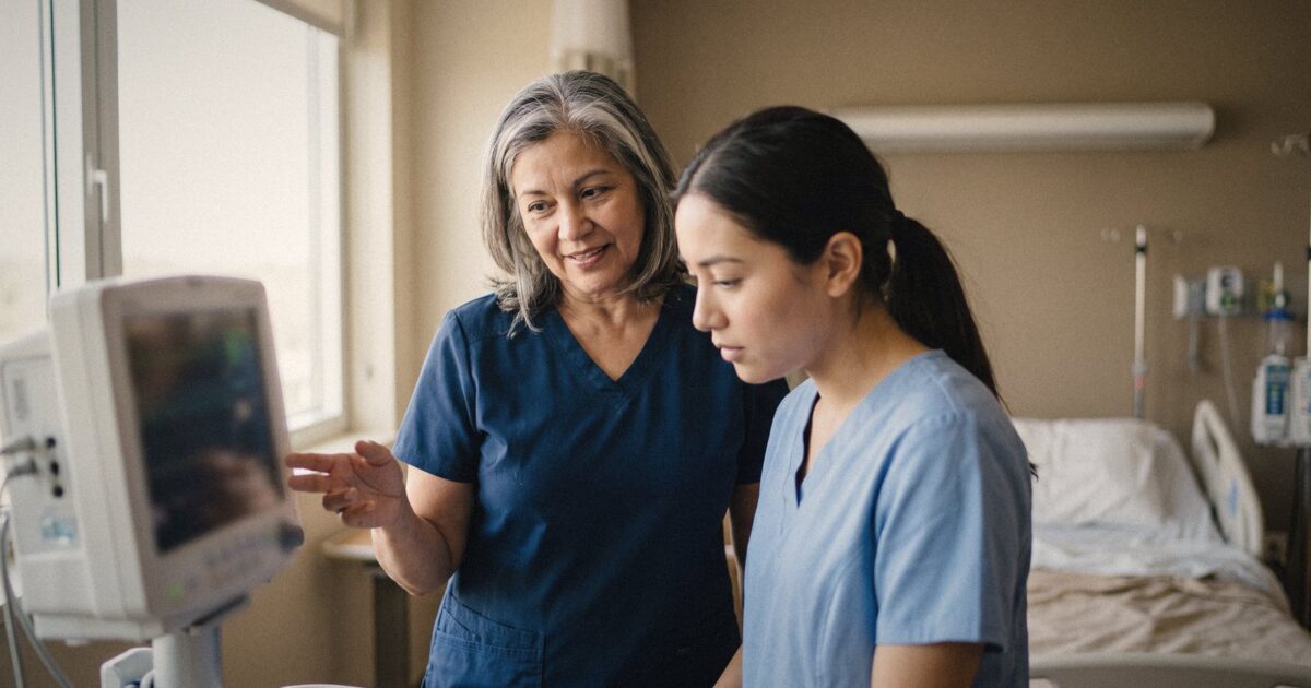 An experienced nurse mentoring a new graduate at a bedside